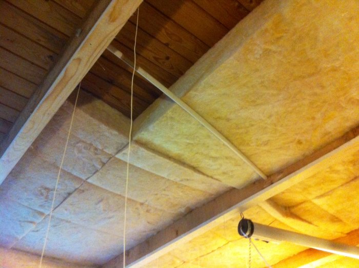 Mineralullsisolering mellan takbjälkar med murarsnören och rör som håller uppe isoleringsmattan.