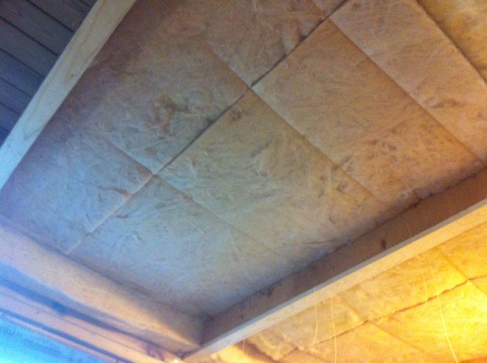 Takisolering med mineralull placerad mellan takbjälkar, som visar minimalt spill och en metod för att hantera isoleringsmattor.