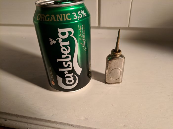 En 33cl Carlsberg burk bredvid en liten oljekanna för storleksjämförelse.