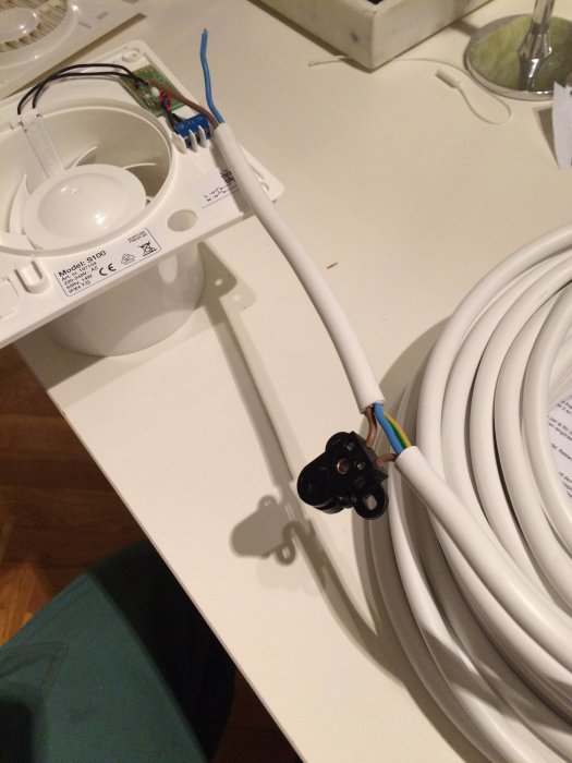 Badrumsfläkt och kabel med kopplingsklämma redo för installation, med anteckning för elarbeten.
