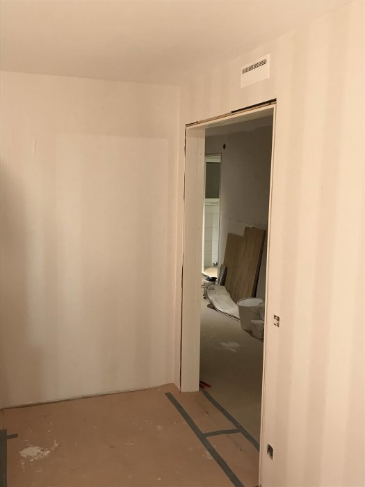 Vardagsrum under renovering med nymålade väggar och skyddsplast på golvet.