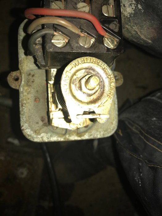 Närbild av en gammal och smutsig elektrisk anslutning med trassliga kablar och en rostig skruvanslutning.