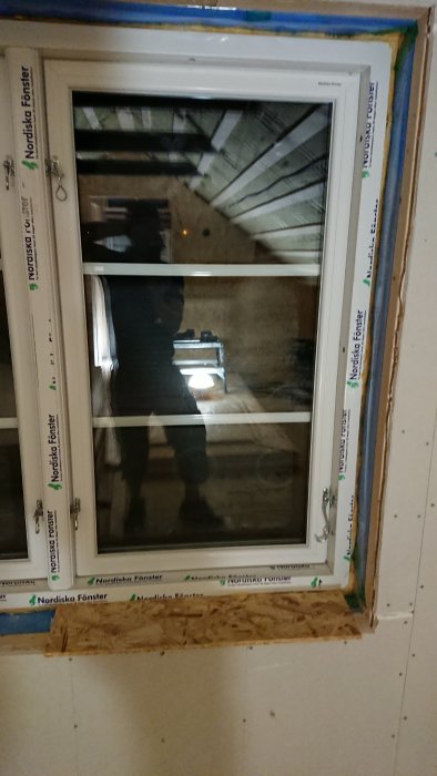 Nyinstallerat fönster med synlig isolering och OSB-skivor i ett underkonstruktionsstadium av en övervåning.