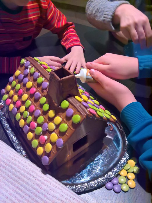 Barn dekorerar ett pepparkakshus med godis och choklad.