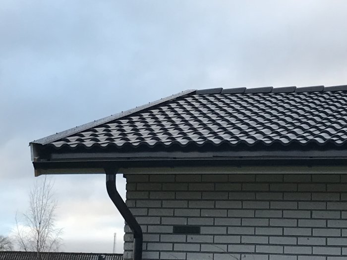 Nya svarta takpannor på hus med synligt glapp mellan nockpanna och vindskivebeslag.