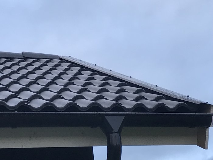 Närbild av takpannor och nockpanna som delvis täcker ett vindskivebeslag, med synligt glapp.