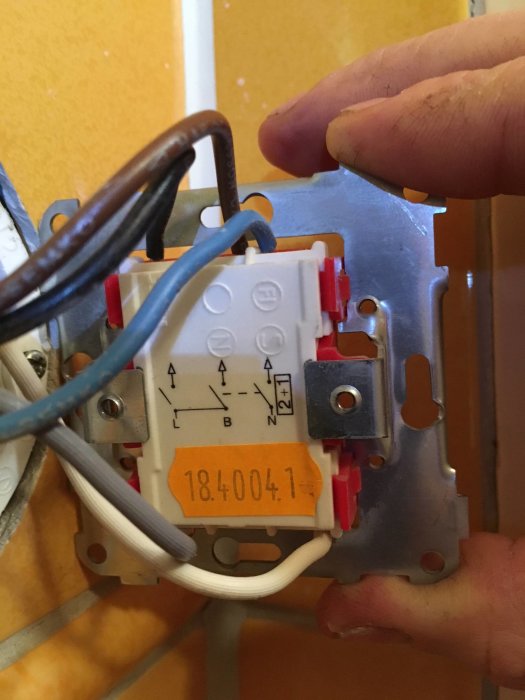 En hand som håller en eldosas bakside med synliga färgade kablar och anslutningar enligt en användares beskrivning av sin elektriska installation.