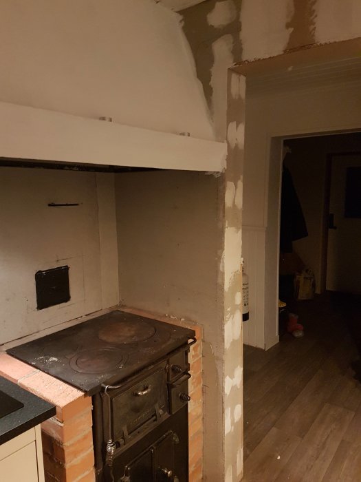Orenoverat kök med spiskåpa över gammal vedspis, putsade väggar delvis förberedda för kakel.
