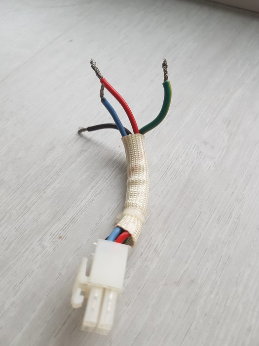 Slutänden av en elkabel med en vit kontakt och urtrådade, färgkodade kablar i rött, blått, grönt och svart på ett vitt underlag.