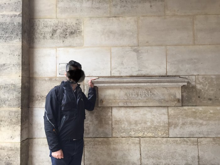 Person står bredvid en stenmätsticka inhuggen i en vägg med texten "METRE".