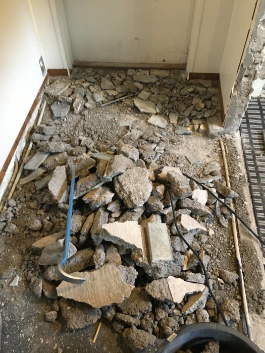 Rivningsarbete av golvyta som resulterat i hög med betongstycken och grus nära vägg och verktyg.