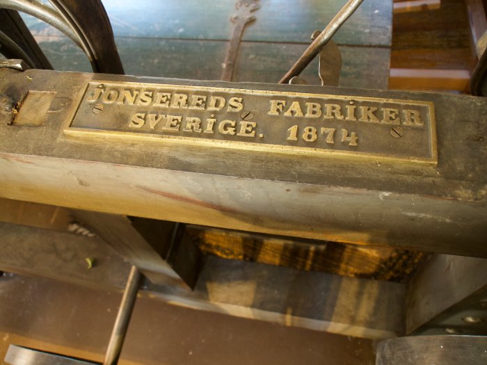 Närbild på en mässingsskylt med ingraverad text "Jonsereds Fabriker Sverige. 1874" på en antik träfundament snickerimaskin.