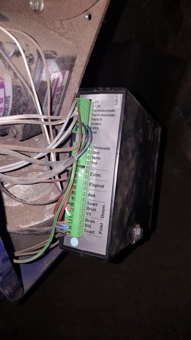 Anslutningsterminal med etiketter och kablar för termostatinstallation, dammig bakgrund.