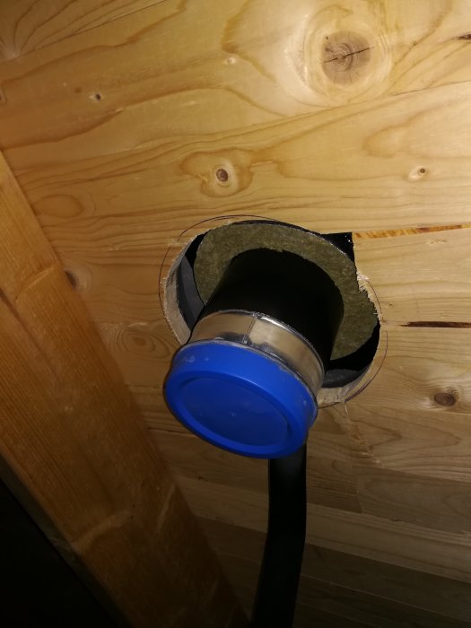 Ventilationsslang monterad i träbjälklag med blått skydd och synlig isolering mot råspont.