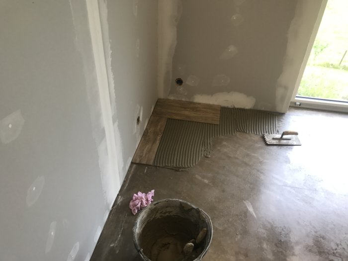 Delvis kaklat golv i ett rum under renovering med spacklade väggar och kakelspik i förgrunden.