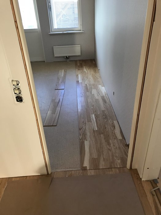 Nyinstallerat laminatgolv i en hall med oavslutat arbete som sträcker sig in i sovrummet.