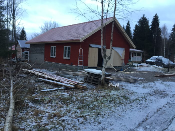 En nybyggd röd byggnad med plåttak, fönster och otäckt väder, byggmaterial framför.