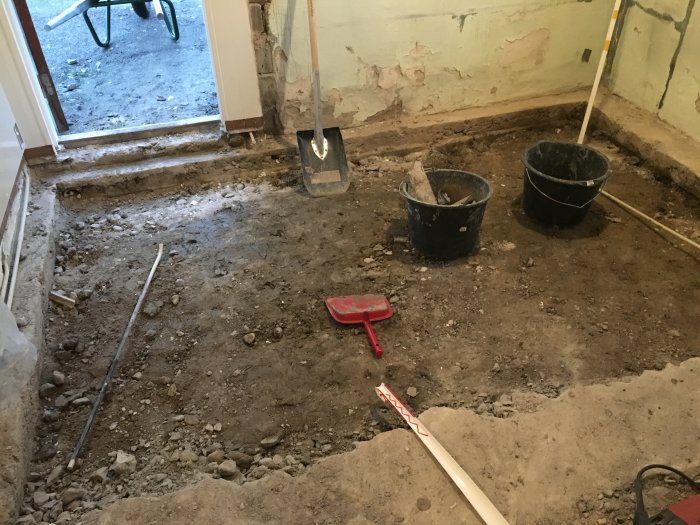 Uppbrutet betonggolv i ett rum med grushög, skottkärra, och verktyg synliga under en renoveringsprocess.