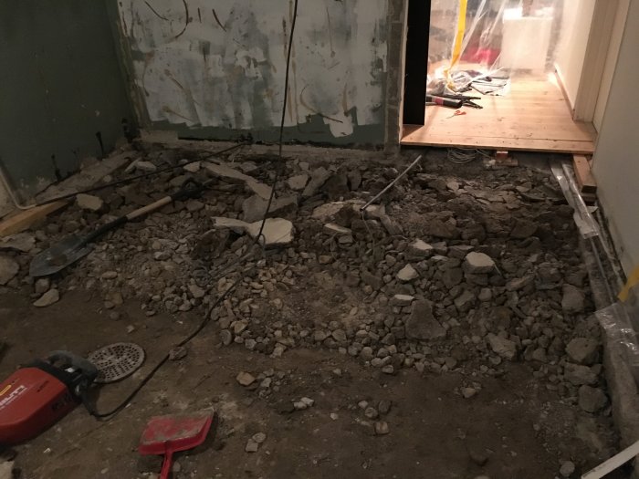 Rum under renovering med uppbilat golv och grushög, verktyg och sladdar syns.