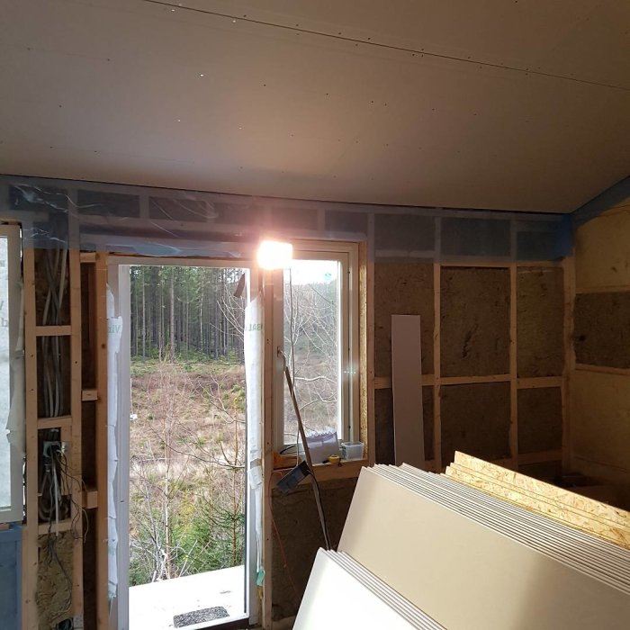 Inredningen av en gäststuga under konstruktion, med isolermaterial på väggen och nymonterade gipsskivor på taket.
