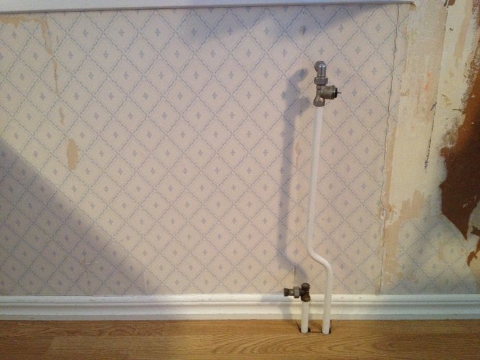 Pluggade rör där en radiator tidigare varit installerad intill en tapetserad vägg och trägolv.