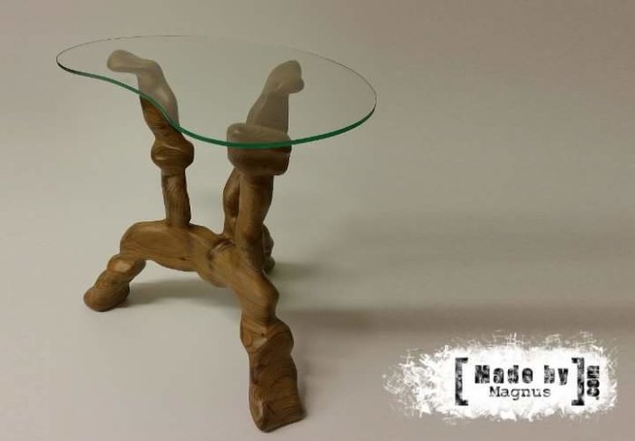 Handgjort litet bord med skulpterade träben och rund glasskiva med logotypen "Made by Magnus".