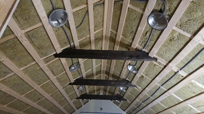 Oisolerat tak med träbjälkar och stenullsisolering. Svarta träplankor och infällda spotlights syns.