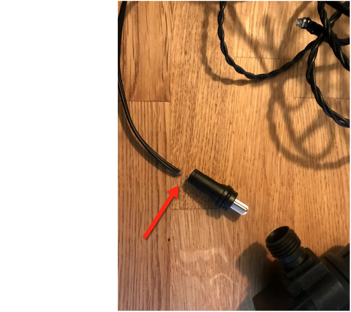 Skadad elektrisk anslutningskontakt på trägolv med en röd pil som pekar på bristande del för lötning.