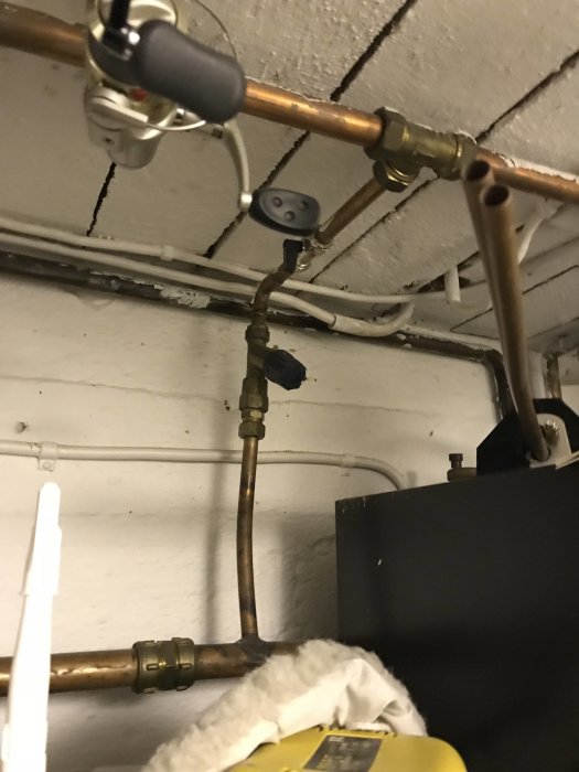 Kopparledningar och ventiler nära en elpanna i ett gammalt värmesystem.