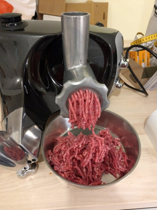 Nymald köttfärs kommer ut från en köttkvarn ner i en rostfri bunke.