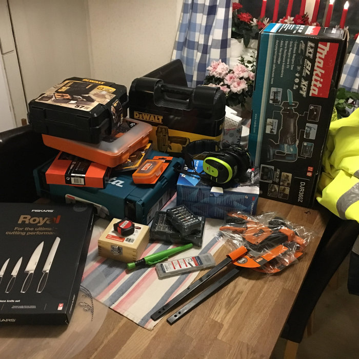 Nyinköpta verktyg och byggmaterial såsom borrmaskin, såg och mätverktyg utspridda på ett bord.