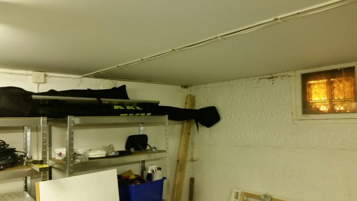 Rörande och skräpigt rum med hyllor, tilluftsventil, eldosor och gammalt fönster.