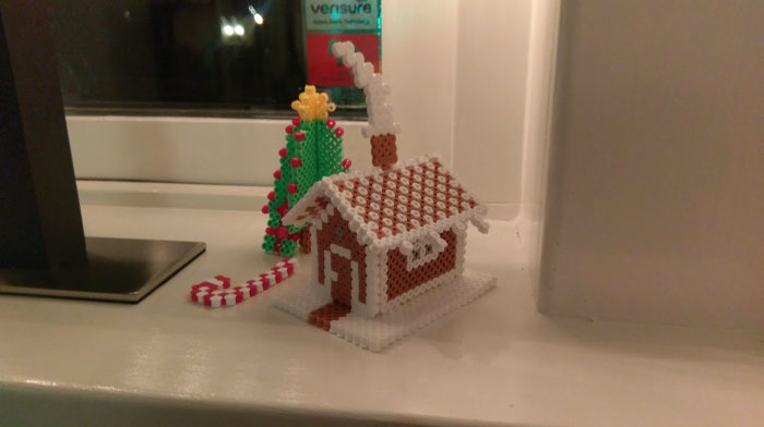 Pepparkakshus och julgran skapade av pärlplattor på en fönsterbräda, nära en surfplatta.