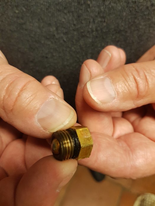 Händer som håller en liten mässingsventil, möjlig säkerhetsventil, med tecken på läckage.