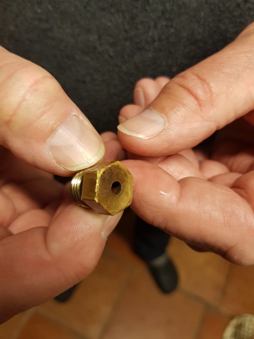 En hand håller en okänd ventil som misstänks vara en säkerhetsventil från ett byggprojekt.