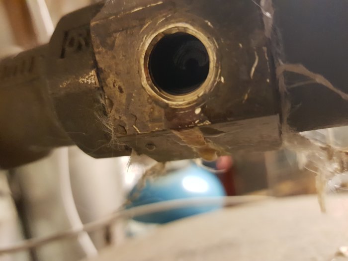 Närbesked av en metallventil som läcker vatten, placerad framför en hydrofon, med tecken på korrosion och avlagringar.