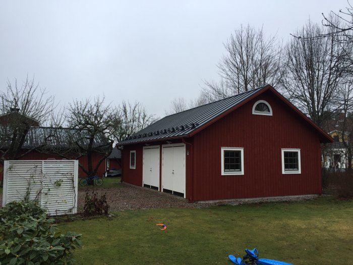 Rött trähus med lösvirke på gavlar, vita fönster utan synlig skarv, svart tak och halvrunt fönster i gavel.