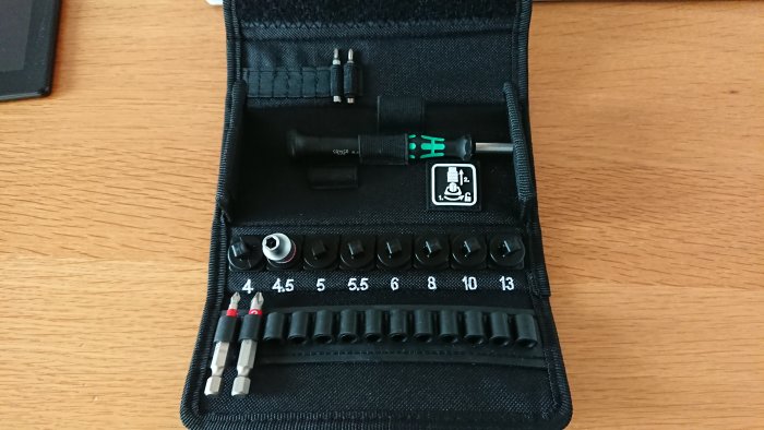 Ett öppet fodral med ordnade hylsor och bits för skruvdragare på ett träbord.