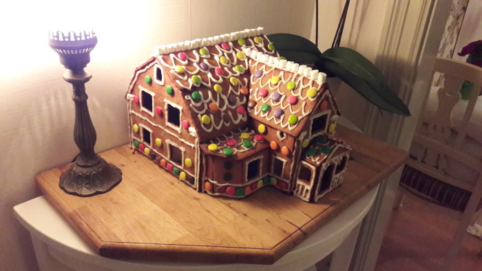 Pepparkakshusmodell av ett utbyggt hus dekorerad med godis på ett skärbräde.