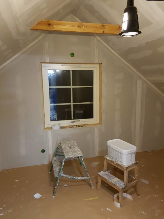 Ett rum under renovering med nylagt golv och spacklade väggar, stegar och målarutrustning syns.