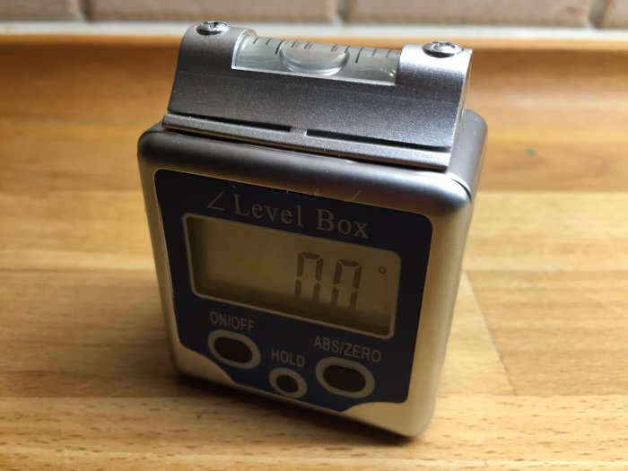 En digital level box med en display som visar vinkelmätning, placerad på ett träbord.