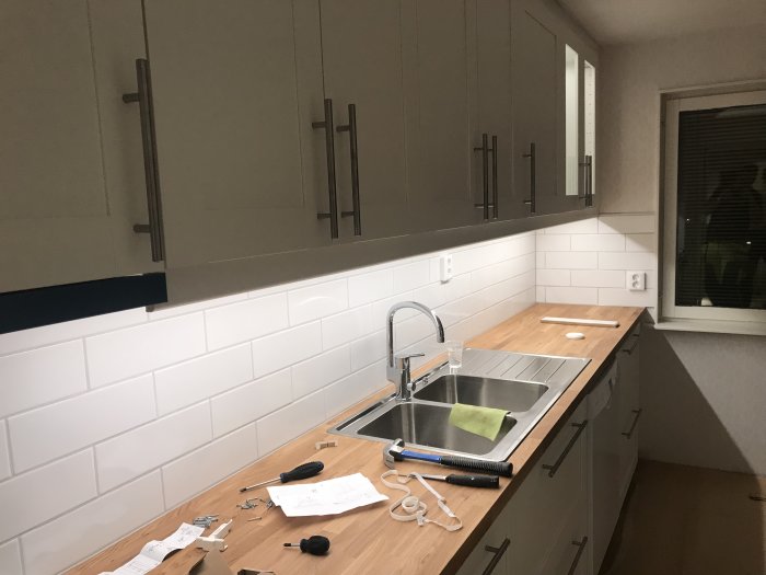 Kök under renovering med nya dekorlisterna installerade, verktyg på arbetsbänken och kakel ovan diskbänk.