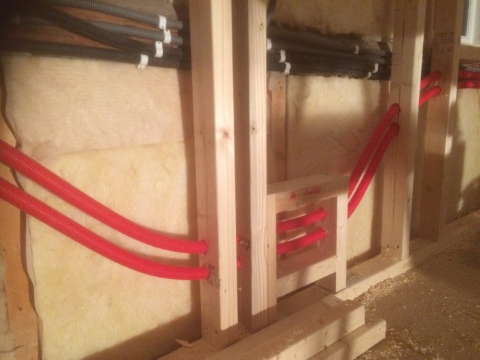 Nyinstallerade vattenrör i rött med framtida anslutningsmöjligheter genom inspektionsluckor i en isolerad väggkonstruktion.