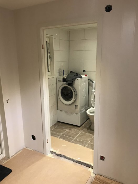 Nyinstallerad vit innerdörr öppnad mot badrum med tvättmaskin och torktumlare.