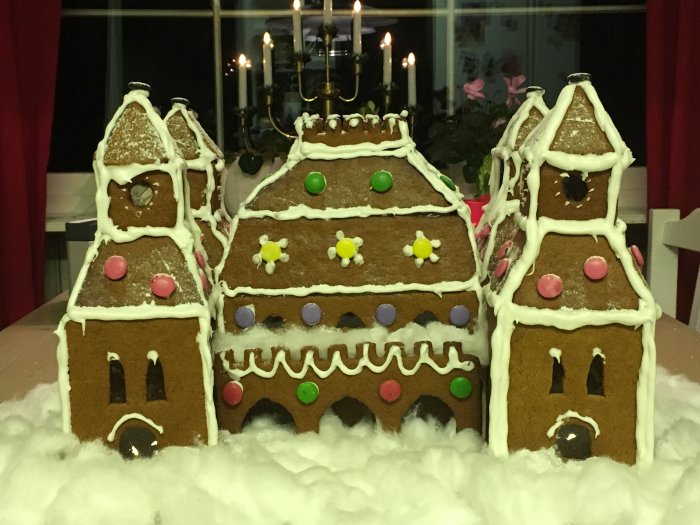 En hemgjord pepparkaksborg dekorerad med glasyr och godis framför ett ljusstake.