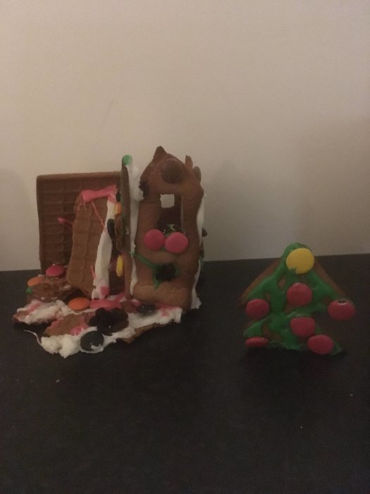 Tre handgjorda pepparkakshus dekorerade med godis på en mörk yta.