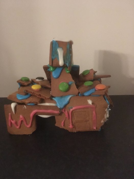 Kreativt pepparkakshus byggt av barn med färgglad glasyr och godisdekorationer.