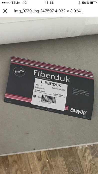 En förpackning EasyUp fiberduk på ett grått golv med en vit väggkant och en synlig trästruktur.