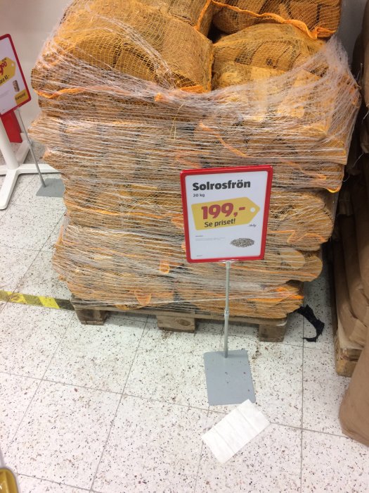 Pall med nätinpackade påsar av solrosfrön för försäljning och skylt som visar pris för 20 kg.