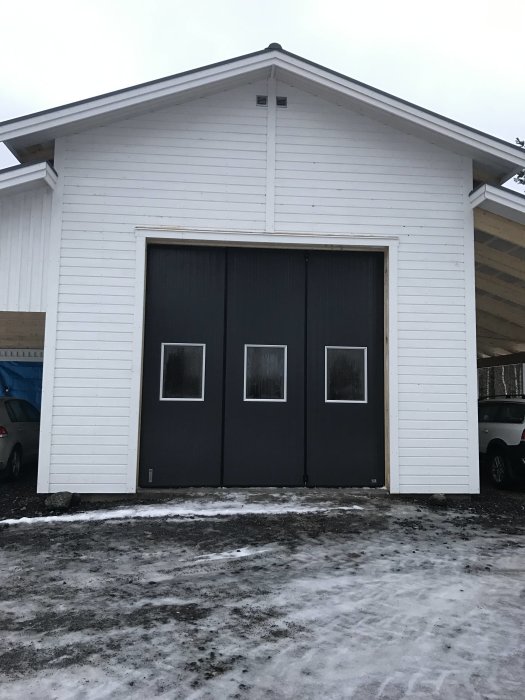 Nybyggt lösvirkes garage med vita väggar och mörka dörrar, med snö och is på marken.